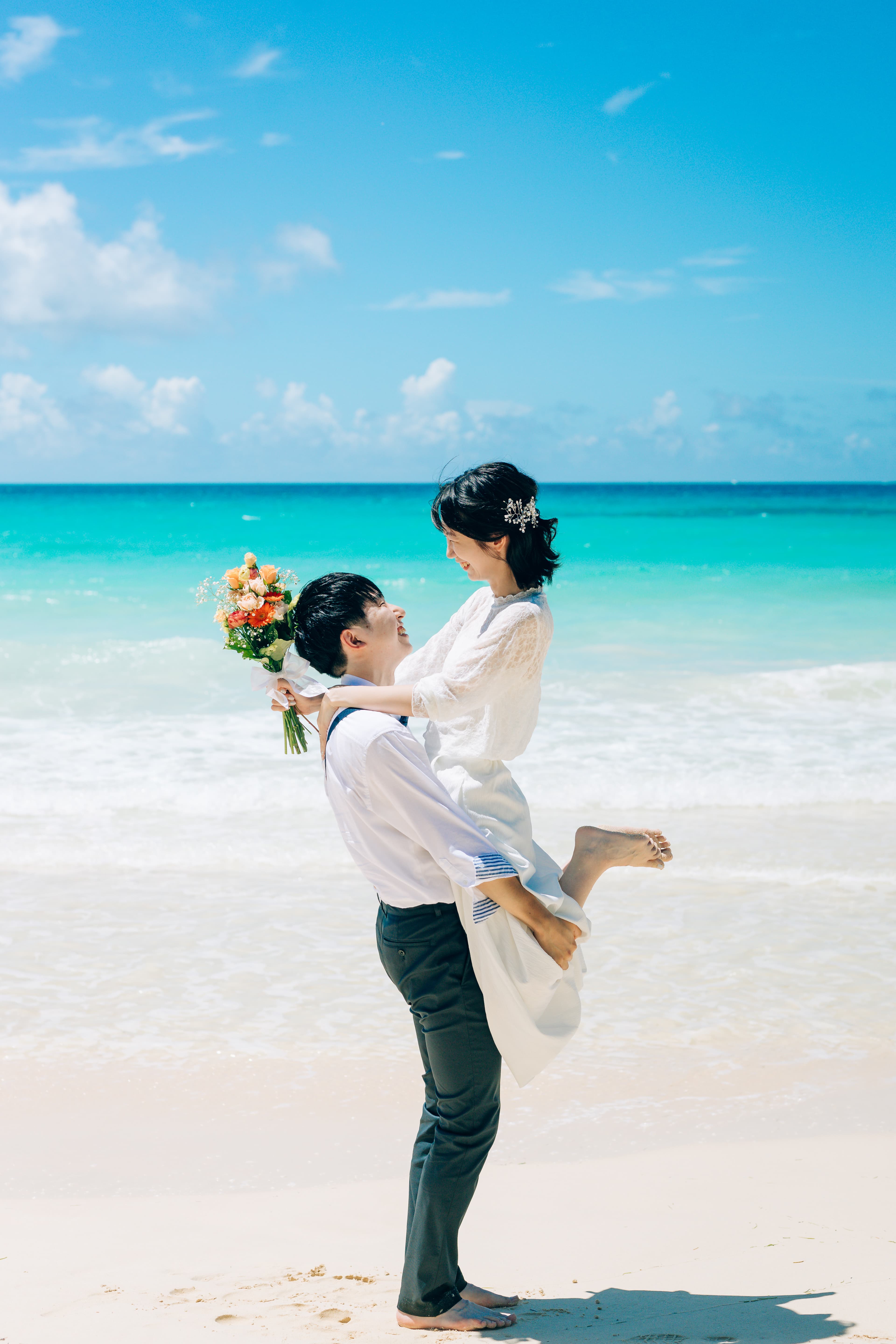宮古島でのカップルフォト撮影：ビーチで花束を持って抱き合う二人